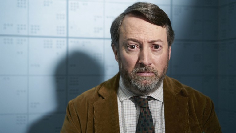 David Mitchell wearing a brown suit, white shirt and tie in BBC One series Ludwig